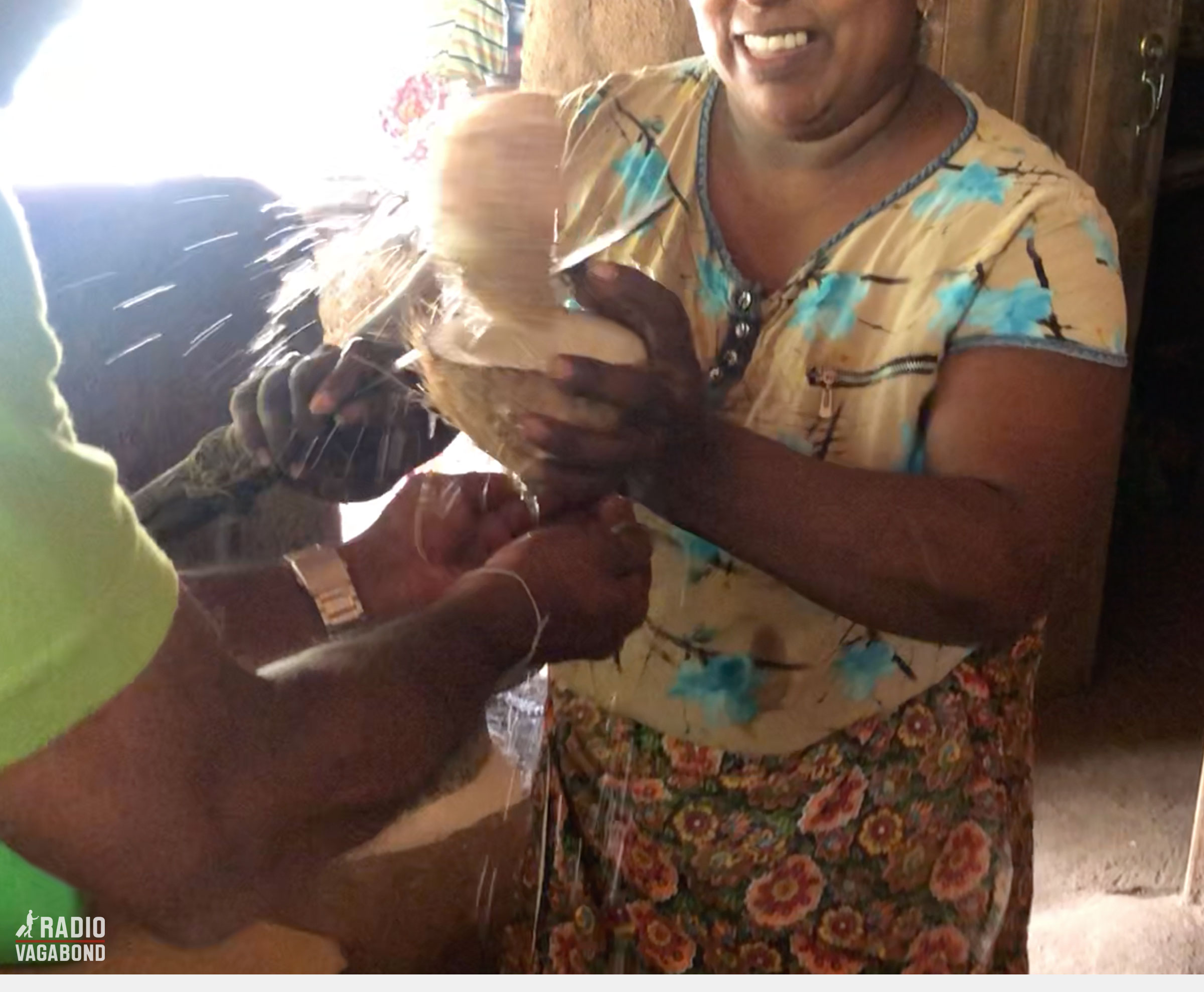 A smiling Sri Lankan woman about to cut a coconut in half with a big knife. 